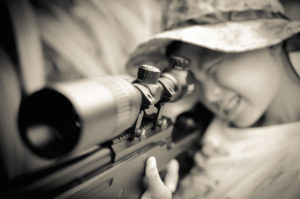 A young child takes aim with a rifle.