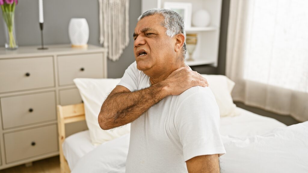 Man sitting on bed holding his shoulder in pain, showing signs of delayed injury after a car accident